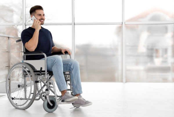 Young man in wheelchair talking on mobile phone near window indoors