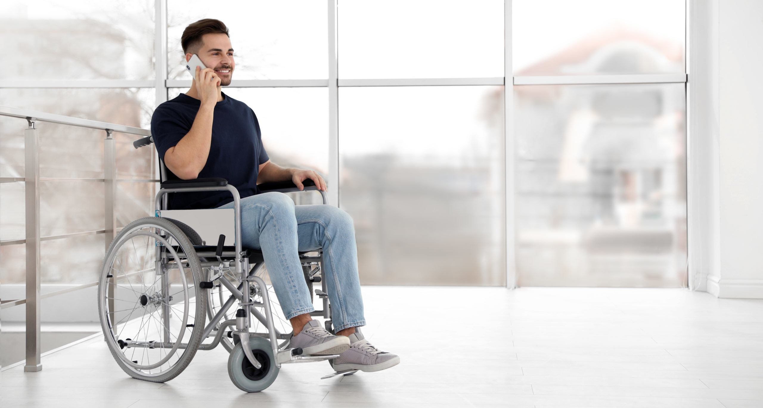 Young man in wheelchair talking on mobile phone near window indoors